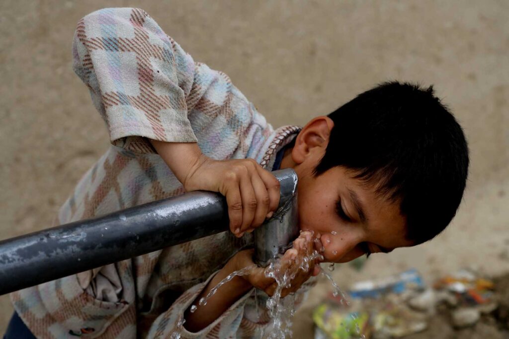 A boy drinking water from an outdoor tap.