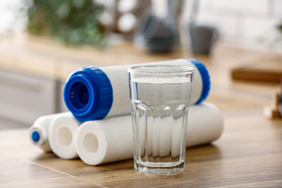 A glass of water with a water filter cartridge behind it.